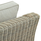 Close-up of the armchair's curved woven arm beside the pale back cushion, showing the open pattern and cushion piping.