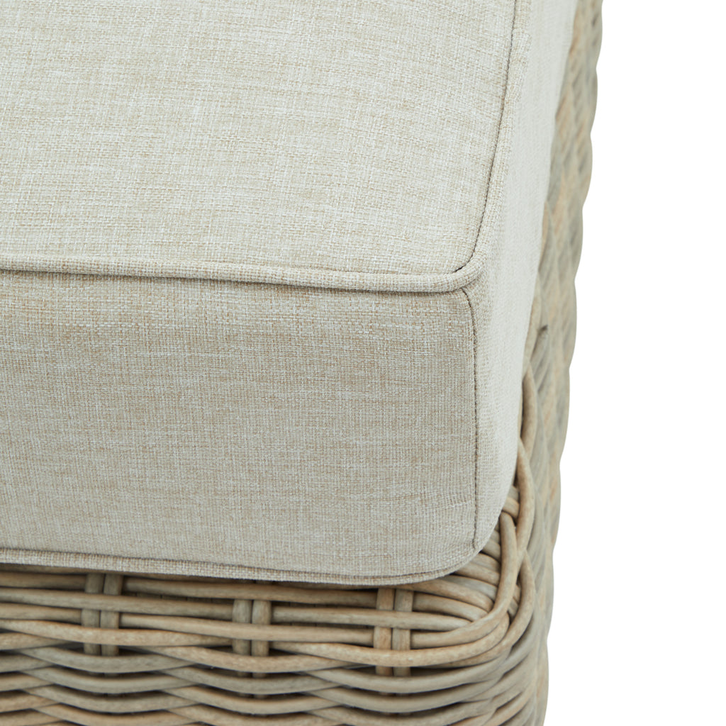 Close-up of the pale cushion's textured fabric and piped corner above the curved weave of the footstool base.