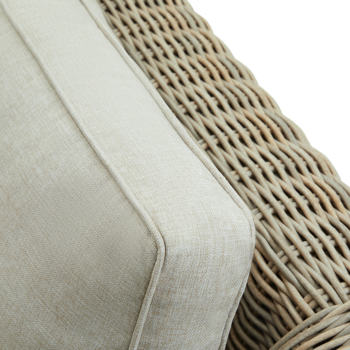 Close-up of a pale cushion's fine fabric texture and piped edge beside the sofa's open grey weave.