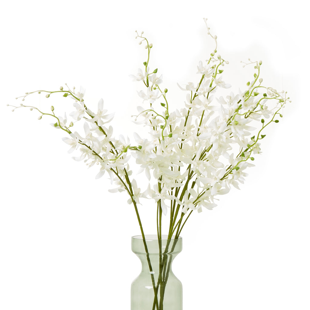 Arrangement of white artificial flowers with spreading green branches in a translucent pale green vase, shown against white.