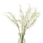 Arrangement of white artificial flowers with spreading green branches in a translucent pale green vase, shown against white.