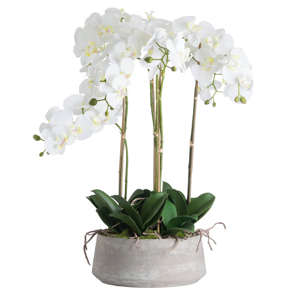 White artificial flower arrangement with arching sprays, green leaves and visible support canes in a low grey oval pot, against a white background.