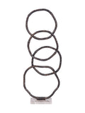 Front view of four overlapping dark, irregular rings standing on a pale rectangular marble base.