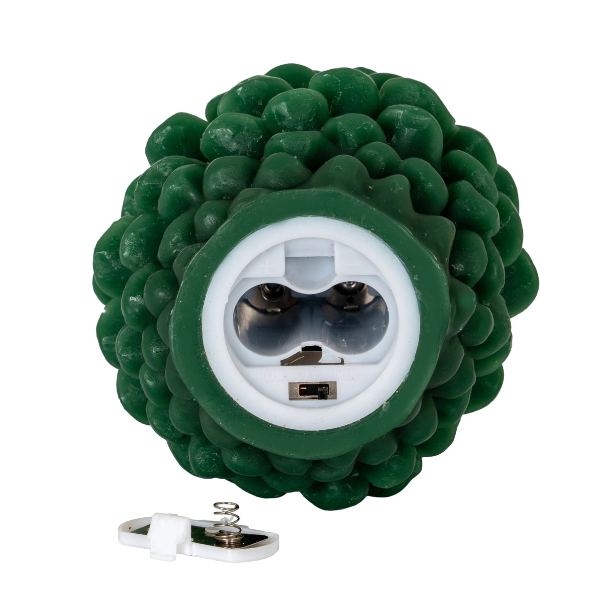 Underside of the green pinecone candle showing an empty white battery compartment and small slide switch, with the removed cover and spring contact below.