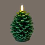 Pinecone LED candle pictured with its flame-shaped element glowing, casting yellow highlights over the upper green scales against a grey background.