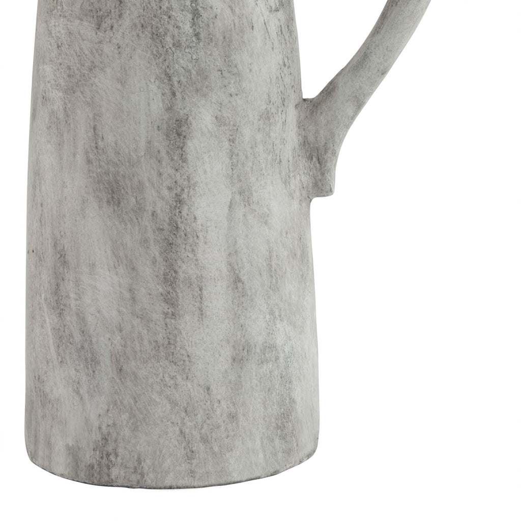 Detail of the jug lower body and base, with grey mottling across the pale surface and the lower handle attachment visible.