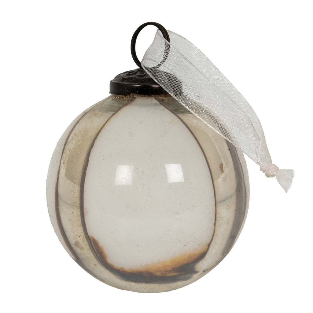 Close view of one round bauble with pale translucent panels, metallic vertical ribs, a warm brown tint at the base and a white sheer ribbon beside its dark cap.