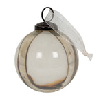 Close view of one round bauble with pale translucent panels, metallic vertical ribs, a warm brown tint at the base and a white sheer ribbon beside its dark cap.