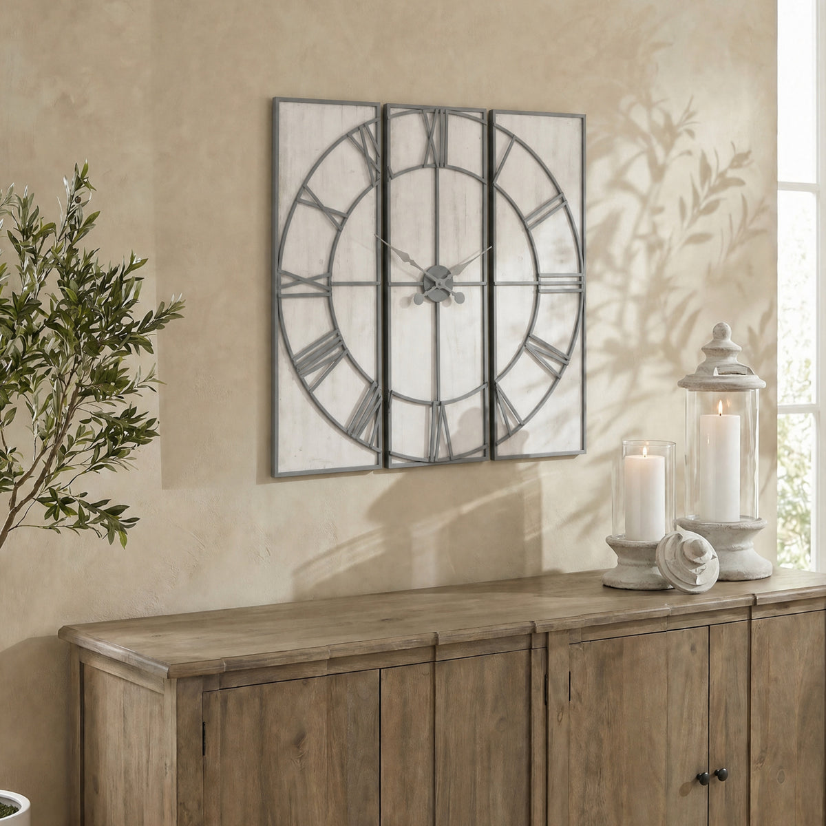 Panel Roman Wall Clock on a warm neutral wall above a wooden sideboard, styled beside foliage and candle lanterns.