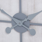Detail of the clock's crossing ornate grey hands and round central cover against the whitewashed surface.