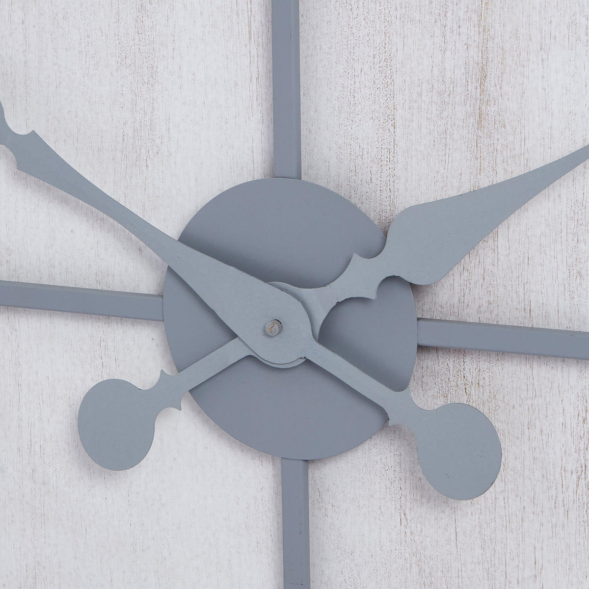 Detail of the clock's crossing ornate grey hands and round central cover against the whitewashed surface.