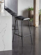 Charcoal stitched bar stools lined along a white veined kitchen island, with dark flooring and woven plant baskets nearby.