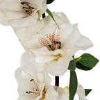 Close-up of pale artificial petals with soft pink edges, rust-coloured throat speckles and black-tipped stamens beside textured green leaves.