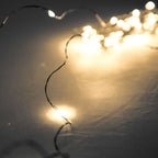 Close-up of fine dark wire with warm-white points of light, curving across a grey surface with blurred lights behind.