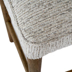 Angled close-up of the padded seat corner, showing textured upholstery, rounded piping and a warm-brown leg below.