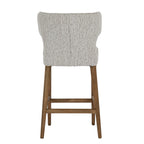 Rear view of the bar stool with a broad curved upholstered back, central seam and warm-brown legs joined by horizontal stretchers.
