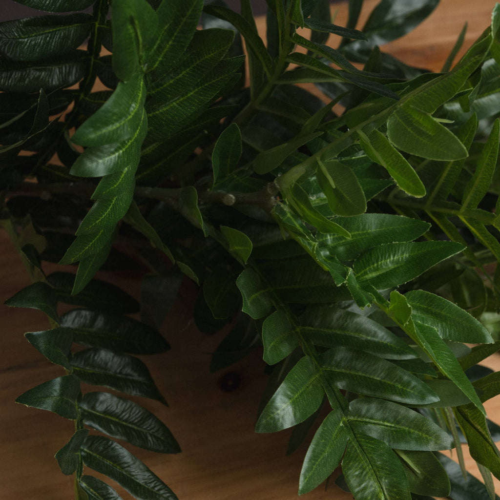 Close-up of pointed artificial green leaflets with lighter central veins and a slight sheen, layered over branching stems.