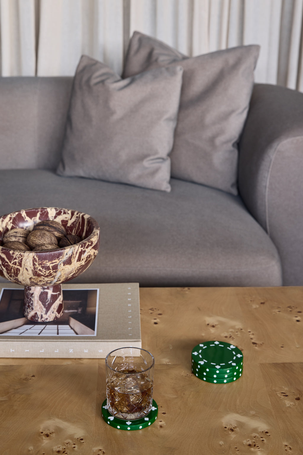 A tumbler on a green poker chip coaster beside the remaining stack on a wooden coffee table in front of a grey sofa.