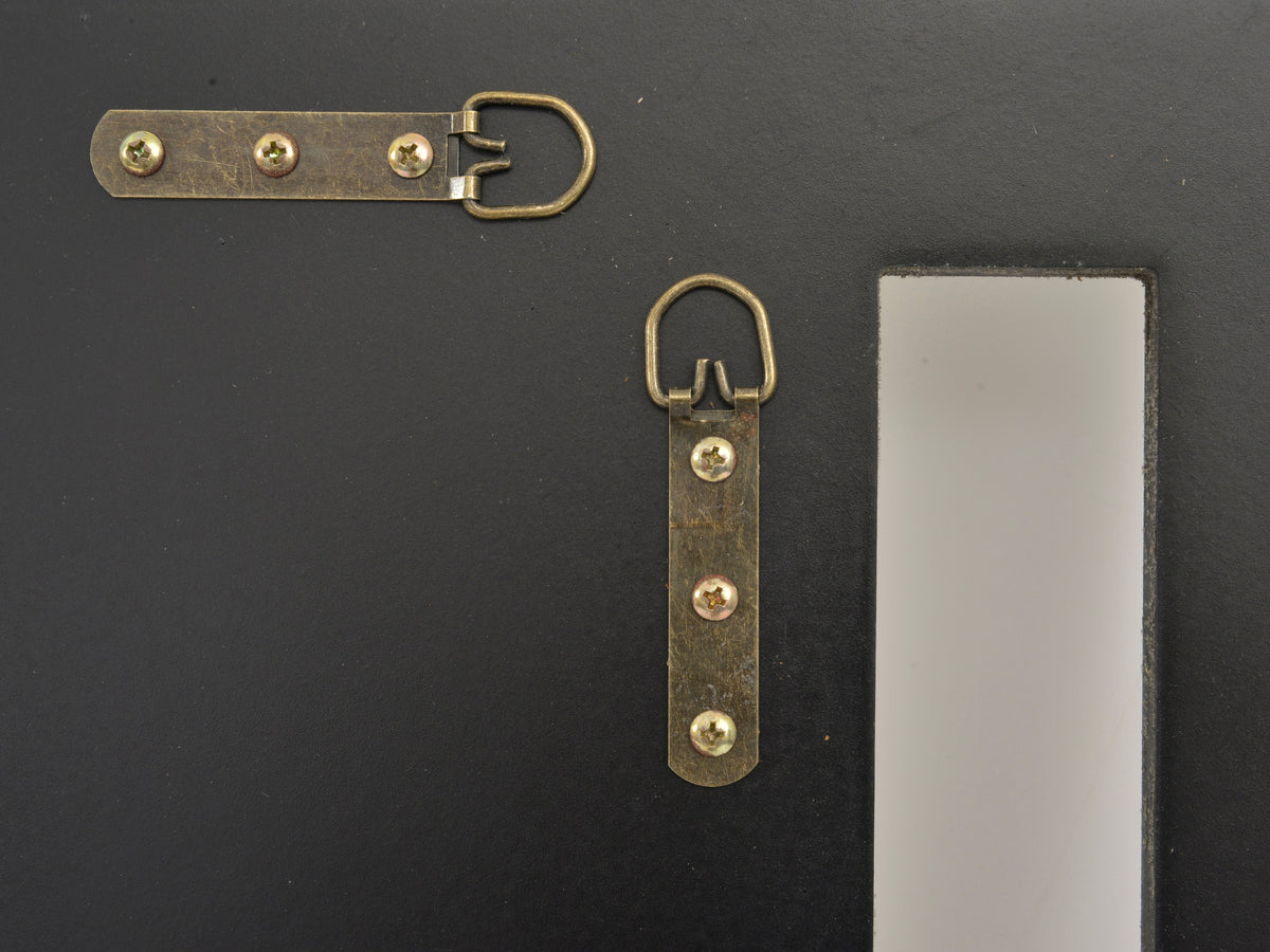 Close-up of the mirror's black rear backing with two metal D-ring strap hangers secured by screws.