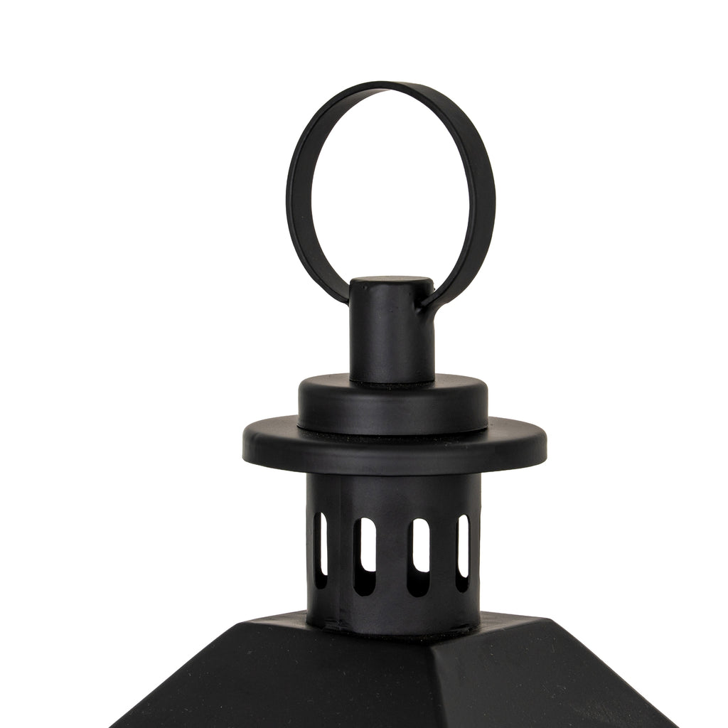 Detail of the black loop ring above the layered circular cap, with elongated slots visible in the cylinder below and the roof edges at the bottom.