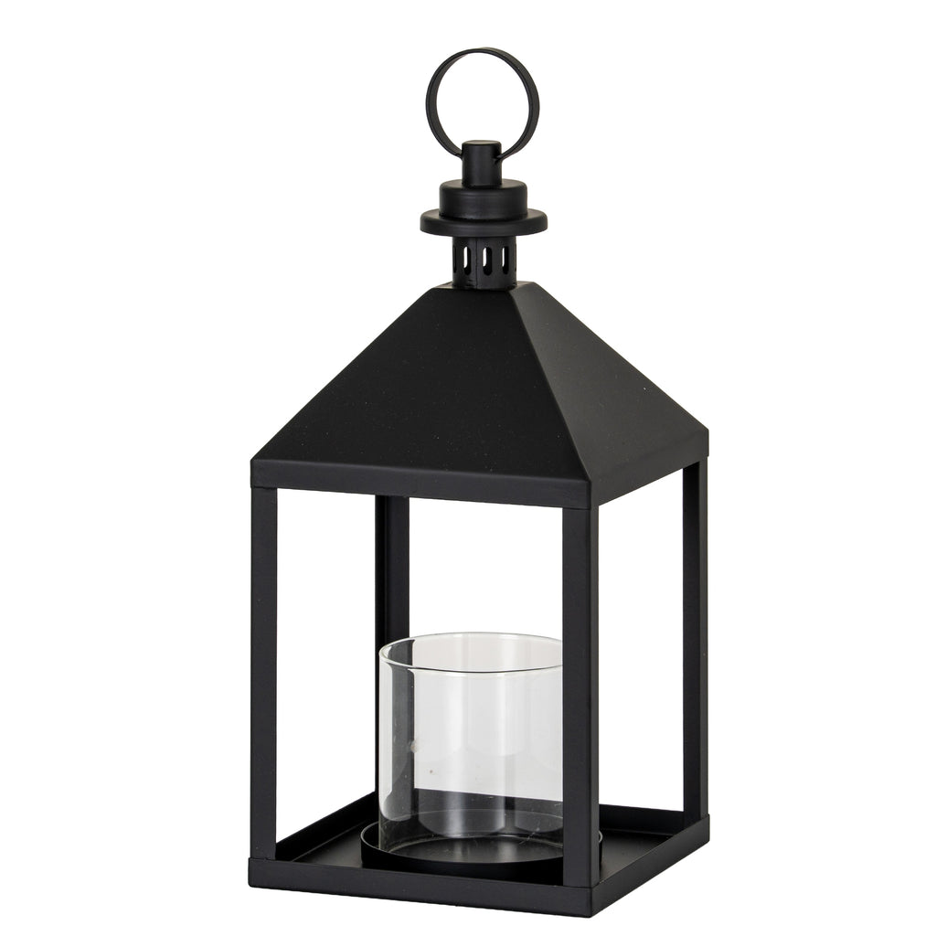 Three-quarter view of a black candle lantern with a square base, four upright posts, clear cylindrical inner holder and pyramidal top beneath a round ring.