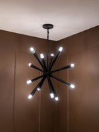 Radiating arm chandelier illuminated beneath a white ceiling in a room with brown panelled walls.