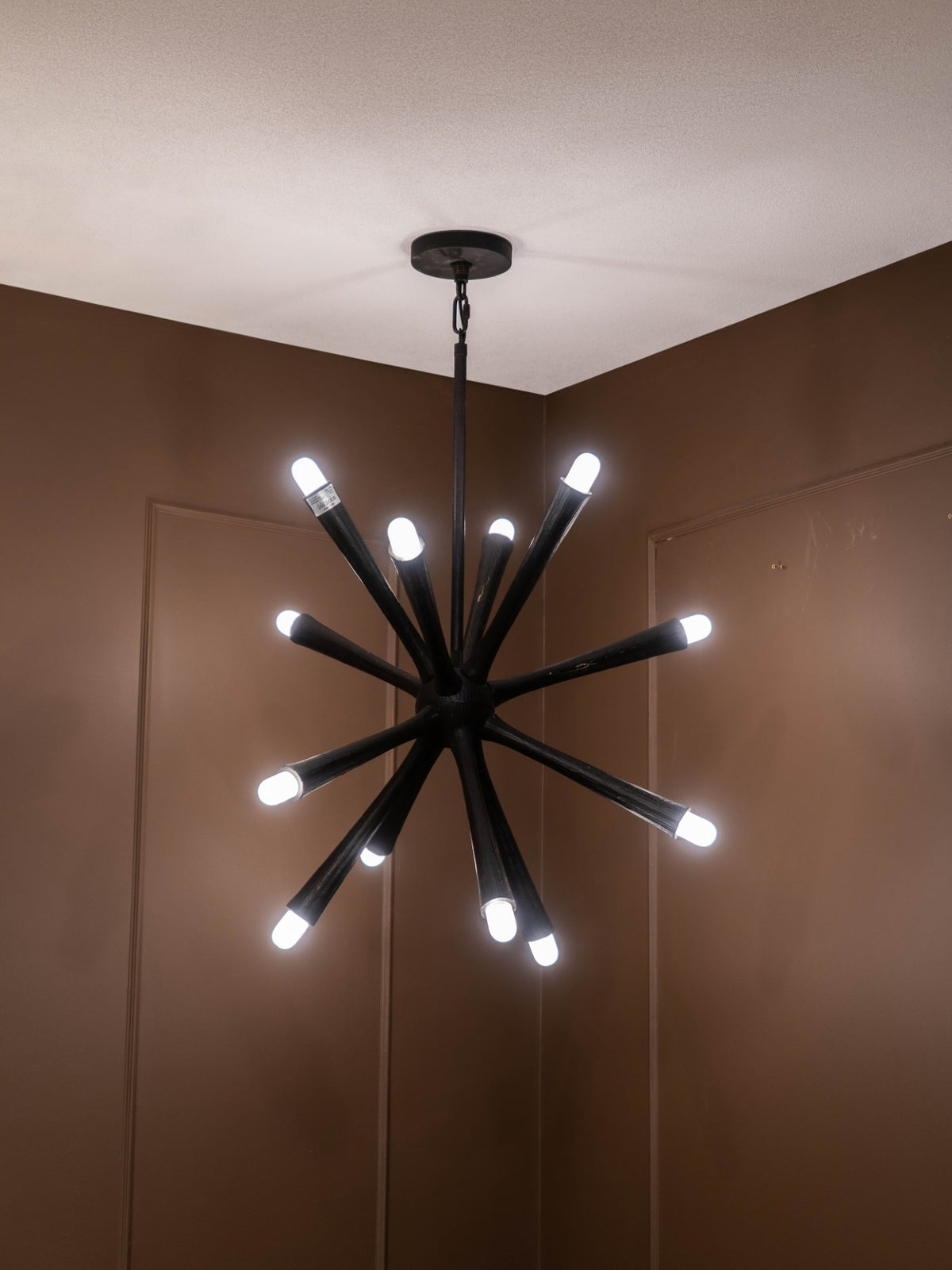 Radiating arm chandelier illuminated beneath a white ceiling in a room with brown panelled walls.