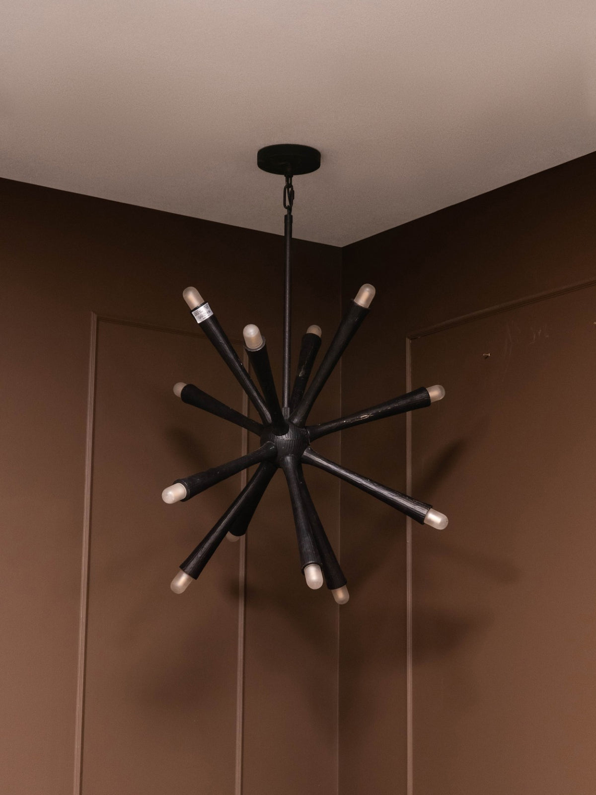Radiating arm chandelier switched off against brown panelled walls, showing dark tapered arms and pale rounded tips.