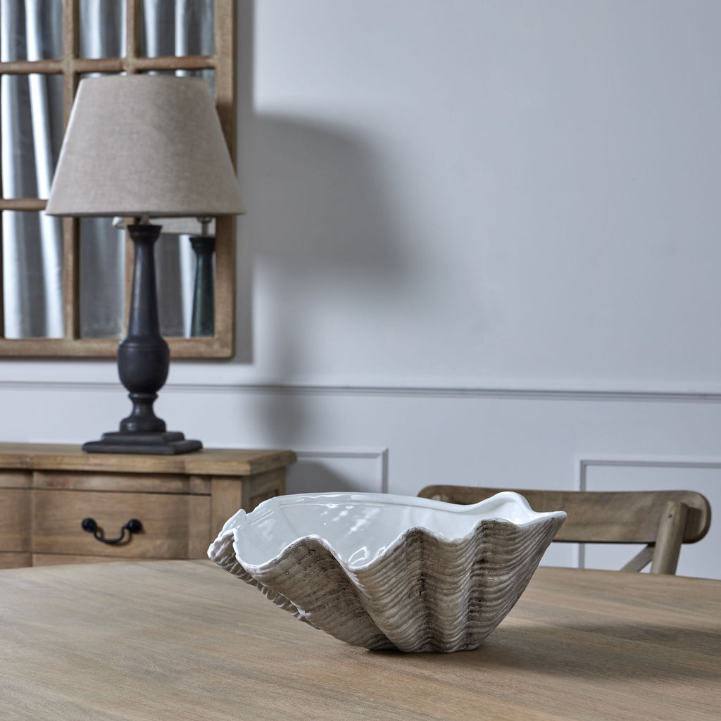 Empty shell planter on a wooden table, with a wooden chair, sideboard, dark table lamp and framed mirror behind it.