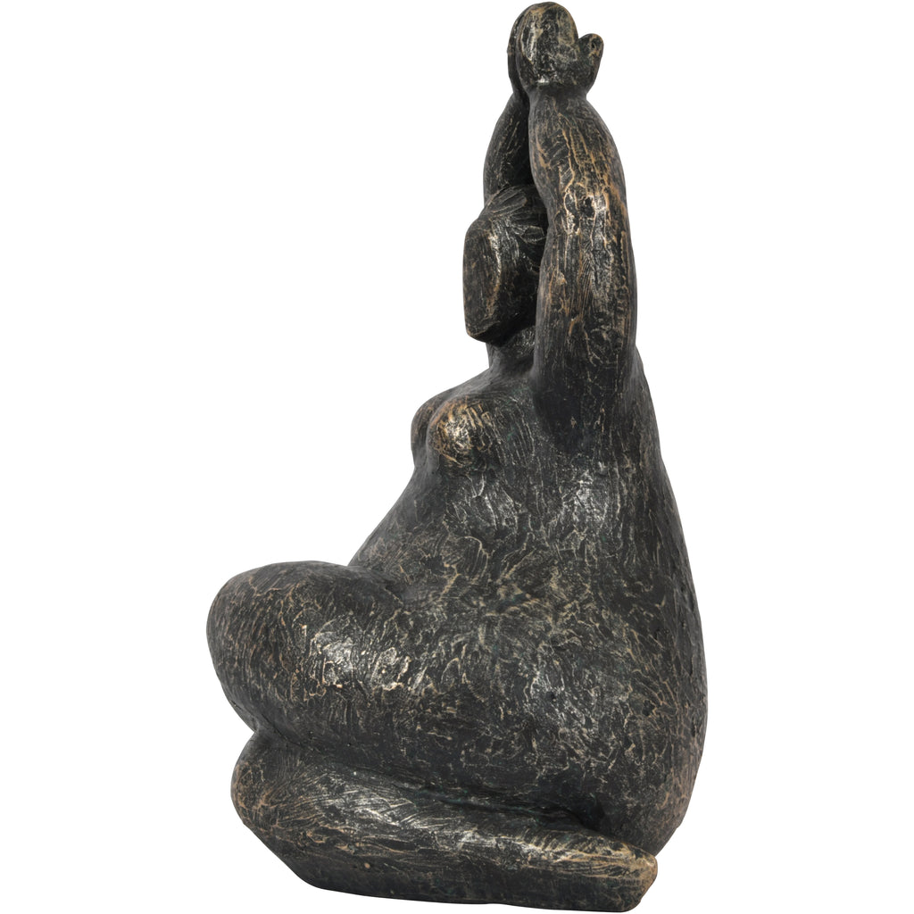 Side view of the seated figure sculpture showing its rounded body, raised arms and distressed bronze surface.