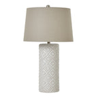 Table lamp with a tall off-white cylindrical base patterned with raised-dot diamonds, a broad neutral tapered shade and rounded silver-coloured finial.