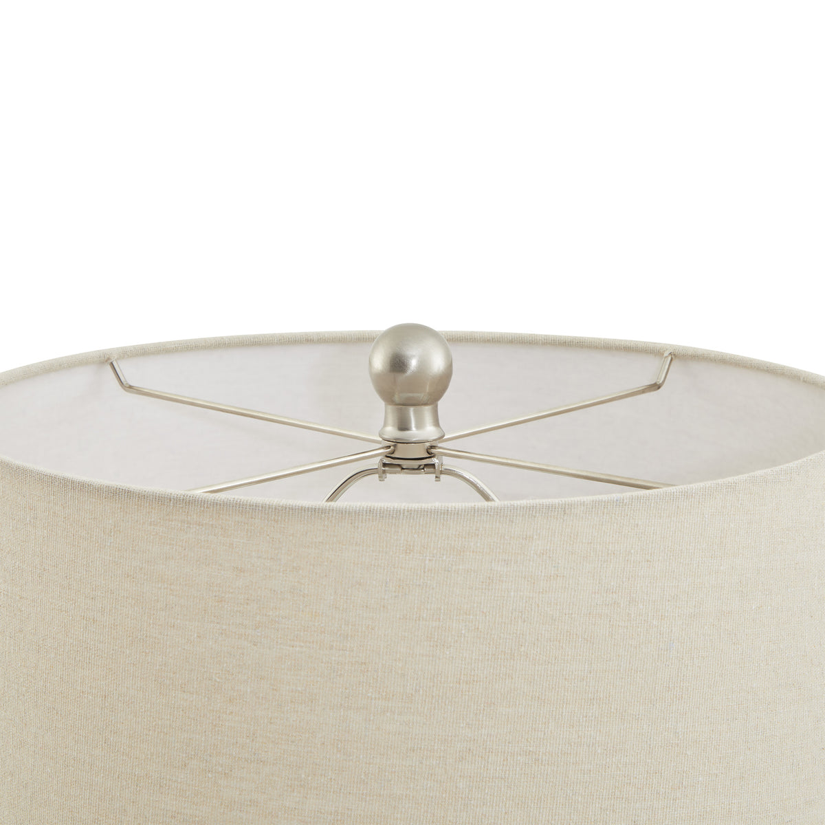 View into the open top of the pale lampshade, showing crossed supports and the round metallic-looking finial.