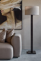 Floor lamp beside a large portrait on a pale wall, with a taupe sofa and neutral cushions beneath the portrait.