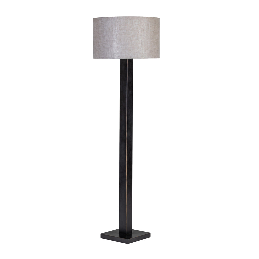 Angled view of the floor lamp showing two faces of its dark stem, warm edging, square base and natural drum shade.