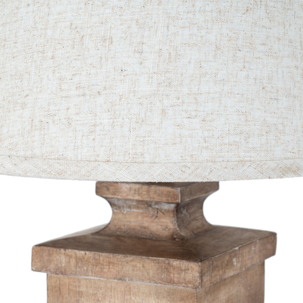 Close-up of the pale shade's woven texture and lower edging above the lamp's warm-brown square shoulder and curved neck.