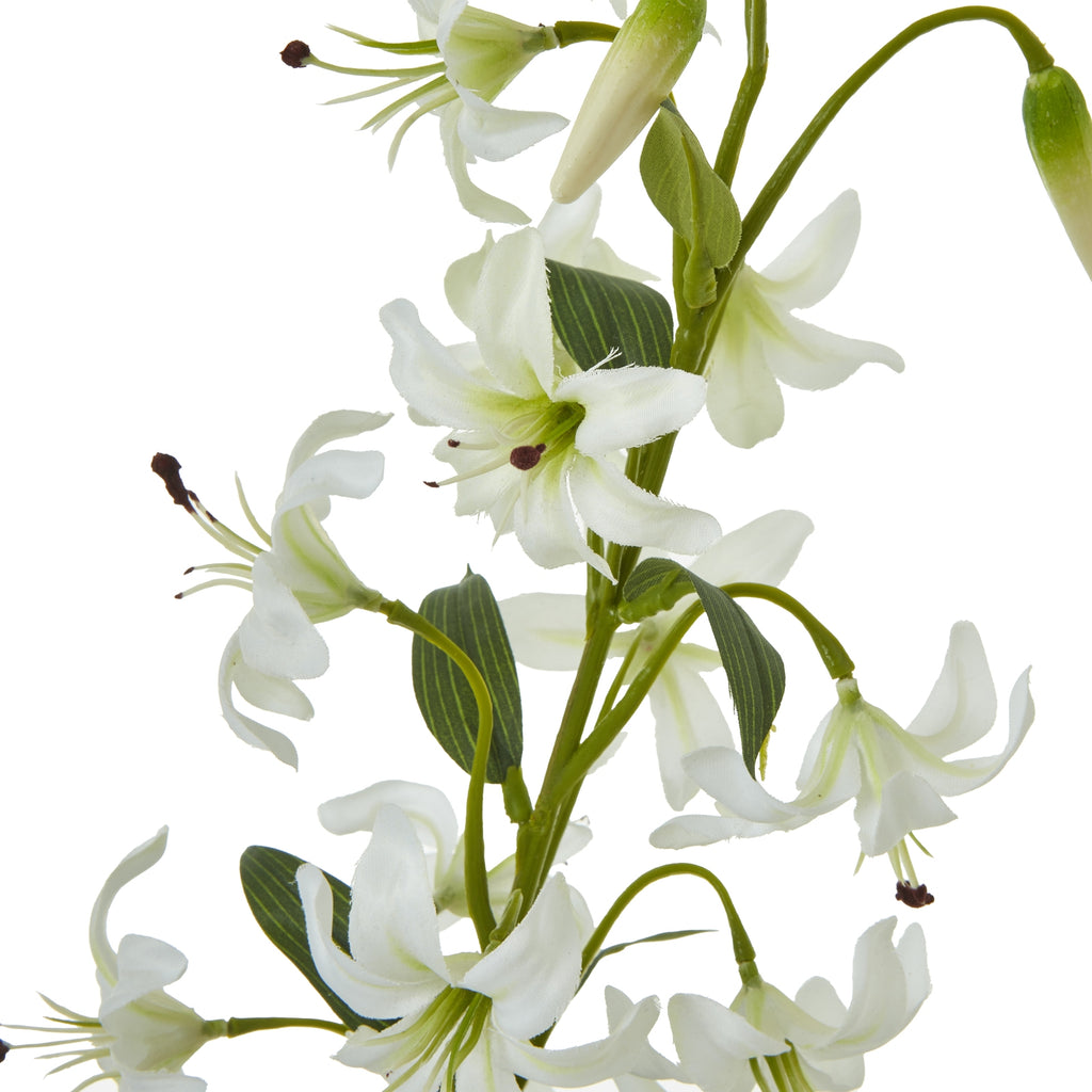 Close-up of white artificial flowers with curled petals, pale green centres and dark-tipped stamens among tapered buds and lined green leaves.