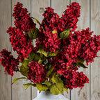 Close view of a vase arrangement filled with red flower clusters and veined green leaves, with the vase rim visible below.