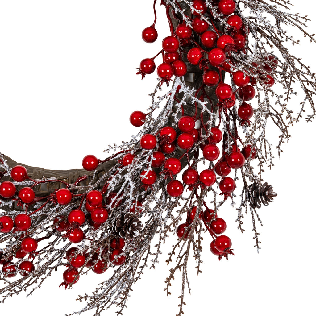 Close-up of the wreath's lower right section, showing shiny red berries, fine frosted branch sprays, pale-tipped brown pinecones and the thick brown ring beneath.