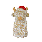 Front view of a seated shaggy cow figure with cream coat lines over a tan body, folded front legs and a red Santa-style hat.