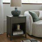Cabinet beside cream upholstered seating, with a ceramic table lamp on top and stacked books and a glass candle holder in the cubby.