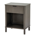 Three-quarter view of the dark grey-brown wooden bedside cabinet, showing its reeded drawer, dark cup pull, open cubby and short turned feet.