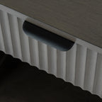 Close-up of the dark cup-shaped drawer pull beneath the wooden top, with vertical reeding across the drawer front.
