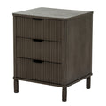 Angled view of the dark grey-brown bedside table showing three reeded drawer fronts, dark cup pulls, a plain side panel and short shaped feet.