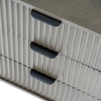 Close-up looking down across the bedside table's vertically ridged drawer fronts and three dark cup-shaped pulls beneath the plain top.