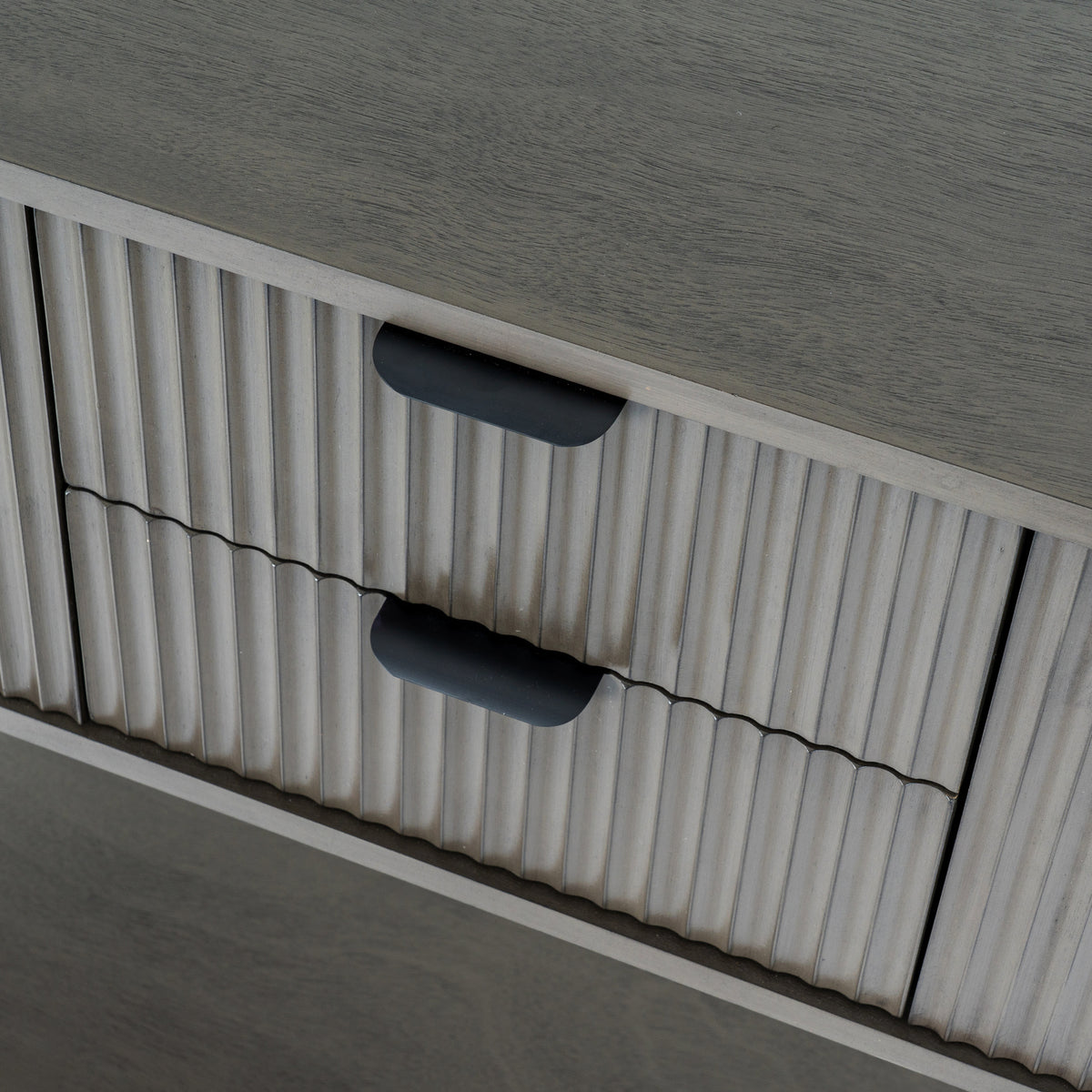 Close-up of the console's two vertically reeded drawer fronts and dark cup-shaped pulls beneath the grain-textured top.
