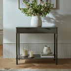 Console table against a pale panelled wall, styled with a white vase of flowering branches on top and glass candle holders, books and a smaller white vase on the lower shelf.