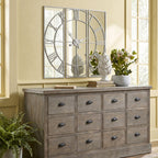 Mirrored Roman-numeral wall clock above a grey drawer sideboard, styled with books, a white ornament and flowers against a pale yellow wall.
