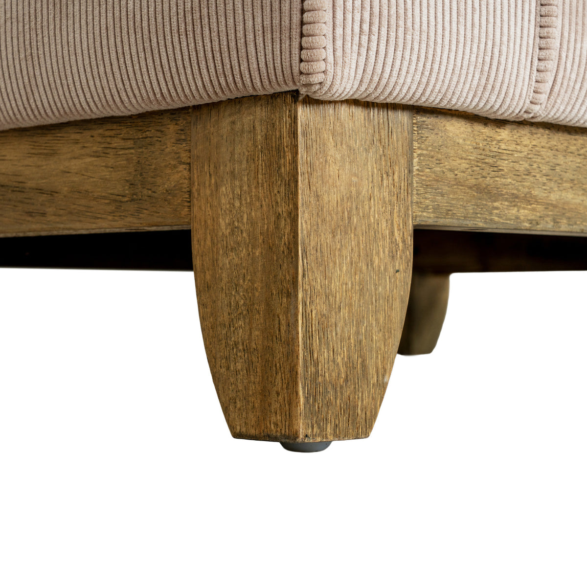 Detail of a brown front foot and adjoining lower rails beneath the cream ribbed upholstery and piped corner.