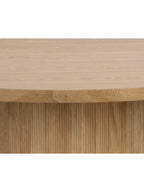 Close-up of the dining table showing wood grain across the top and chamfered edge above the vertically grooved pedestal.