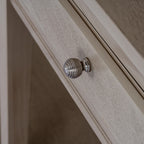 Close-up of a rounded silver-coloured ribbed knob against the pale grained drawer front and its bevelled border.